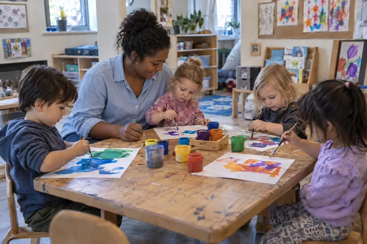 A teacher helping a small group of children paint at a classroom table